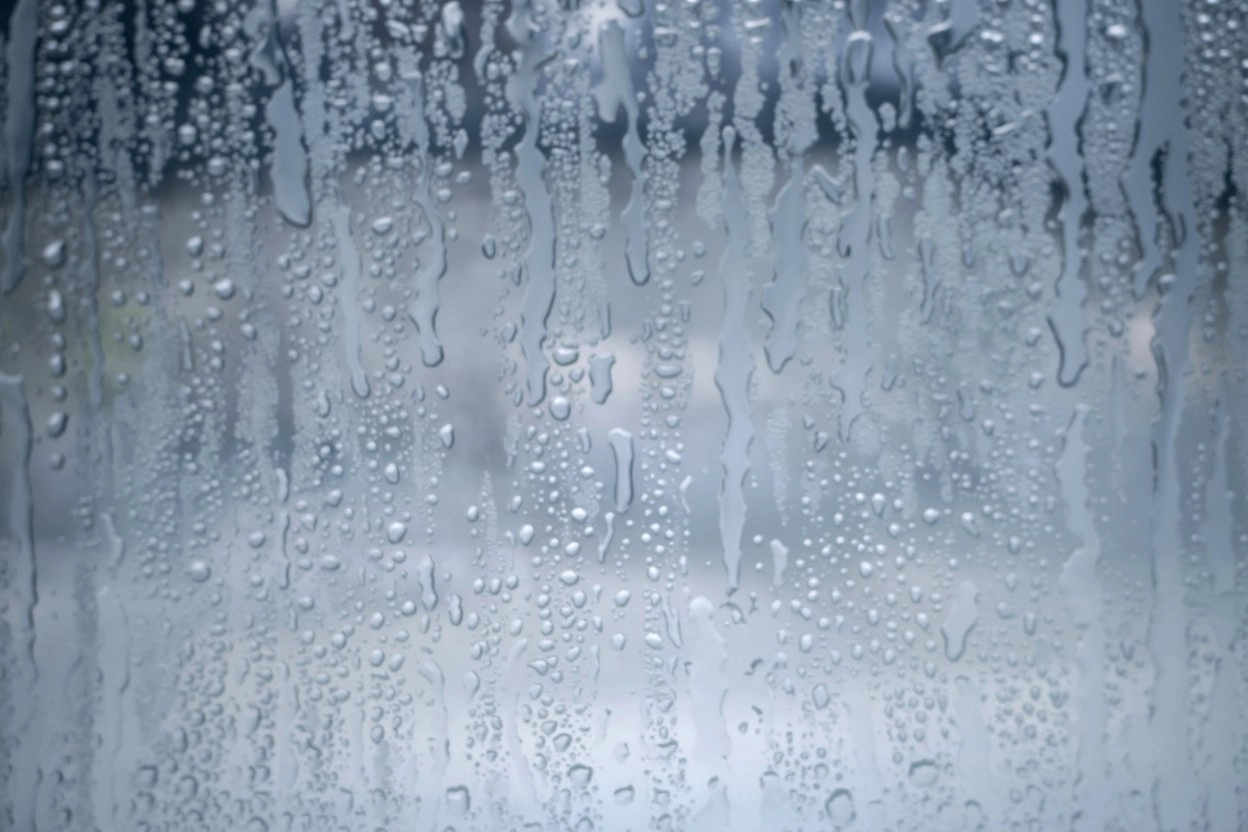 A close-up photograph of condensation droplets on a window pane. rethink your windows 