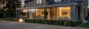 in the golden tail of dusk, a british home with panoramic architectural glazing radiates modern serenity. each window pane captures the last light of day, while the interior glows in balanced layers — downlights along the ceiling,